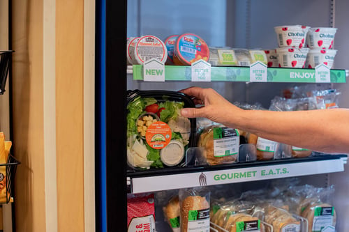 hand reaching into micro market cooler pulling out a packaged salad