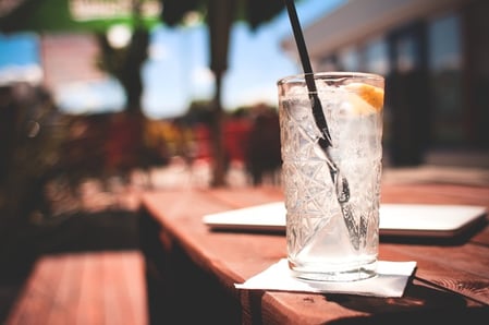 glass of water with a straw and lemon sitting outside on a sunny picnic table