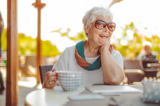 Older woman smiling and drinking coffee outdoors