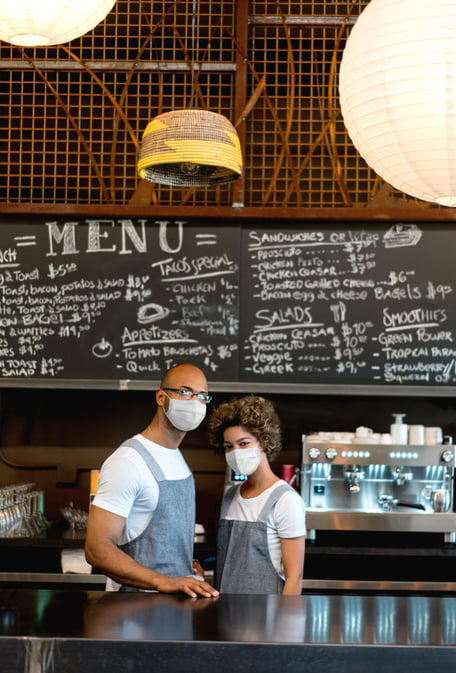 Two employees working behind the counter at a restaurant with masks on