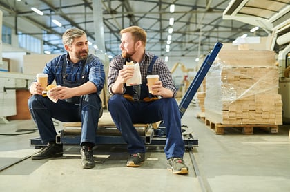 Two male employees on a break in warehouse eating lunch 