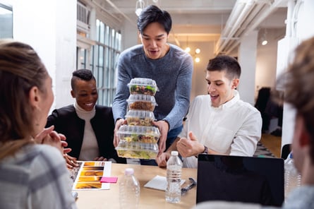 Coworkers at a group table being presented with lunch in clear containers